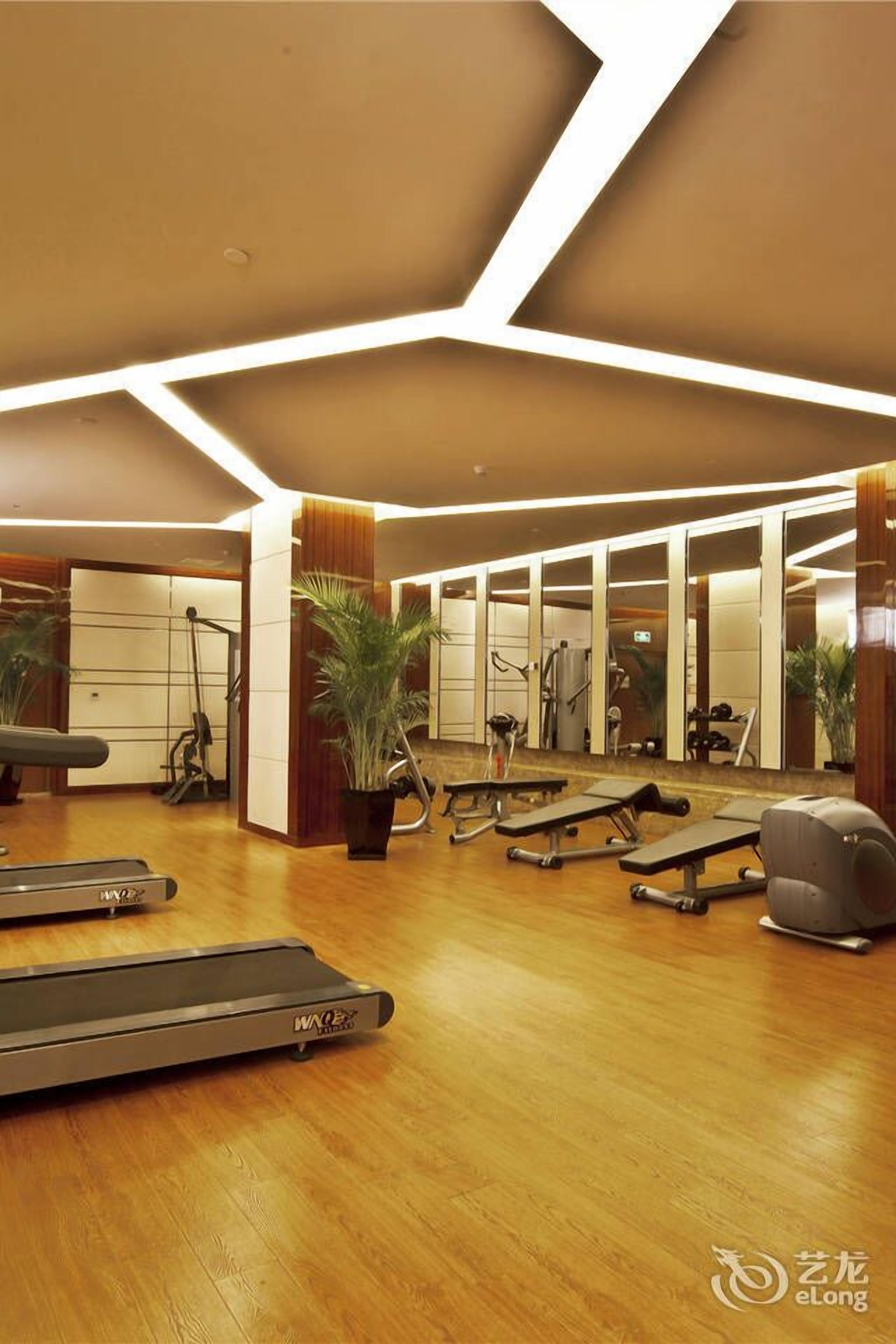 Un gimnasio con cintas de correr, equipo de ejercicio y suelo de madera.