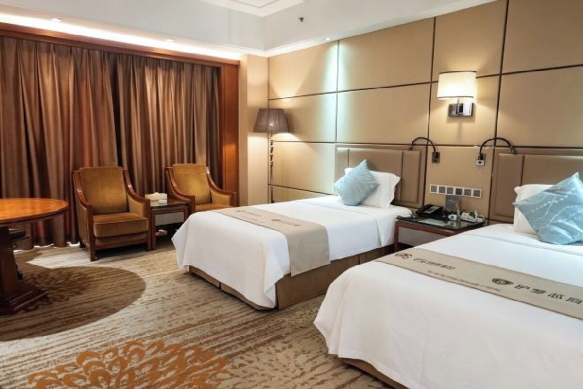 A hotel room with two beds, a desk, a chair, a lamp, and a curtain.