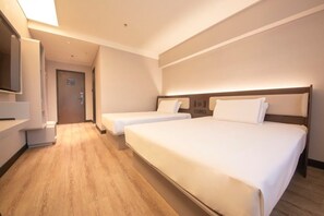 Una habitación de hotel con una cama grande, una cama más pequeña, un televisor y suelo de madera.