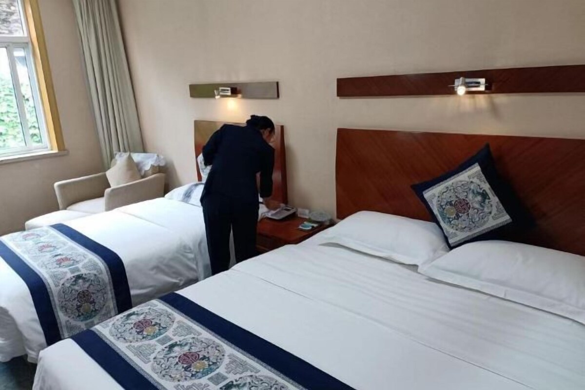 A hotel room with two beds, a nightstand, a chair, and a window with curtains.