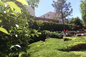 A well-maintained garden with various plants and flowers, a pathway, and a building in the background. - Longshan Hotel (Handan)