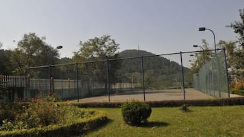 Una cancha de tenis cercada, con cielo despejado y árboles al fondo.