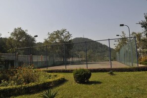 Un court de tennis entouré de clôtures, avec un ciel dégagé et des arbres en arrière-plan.