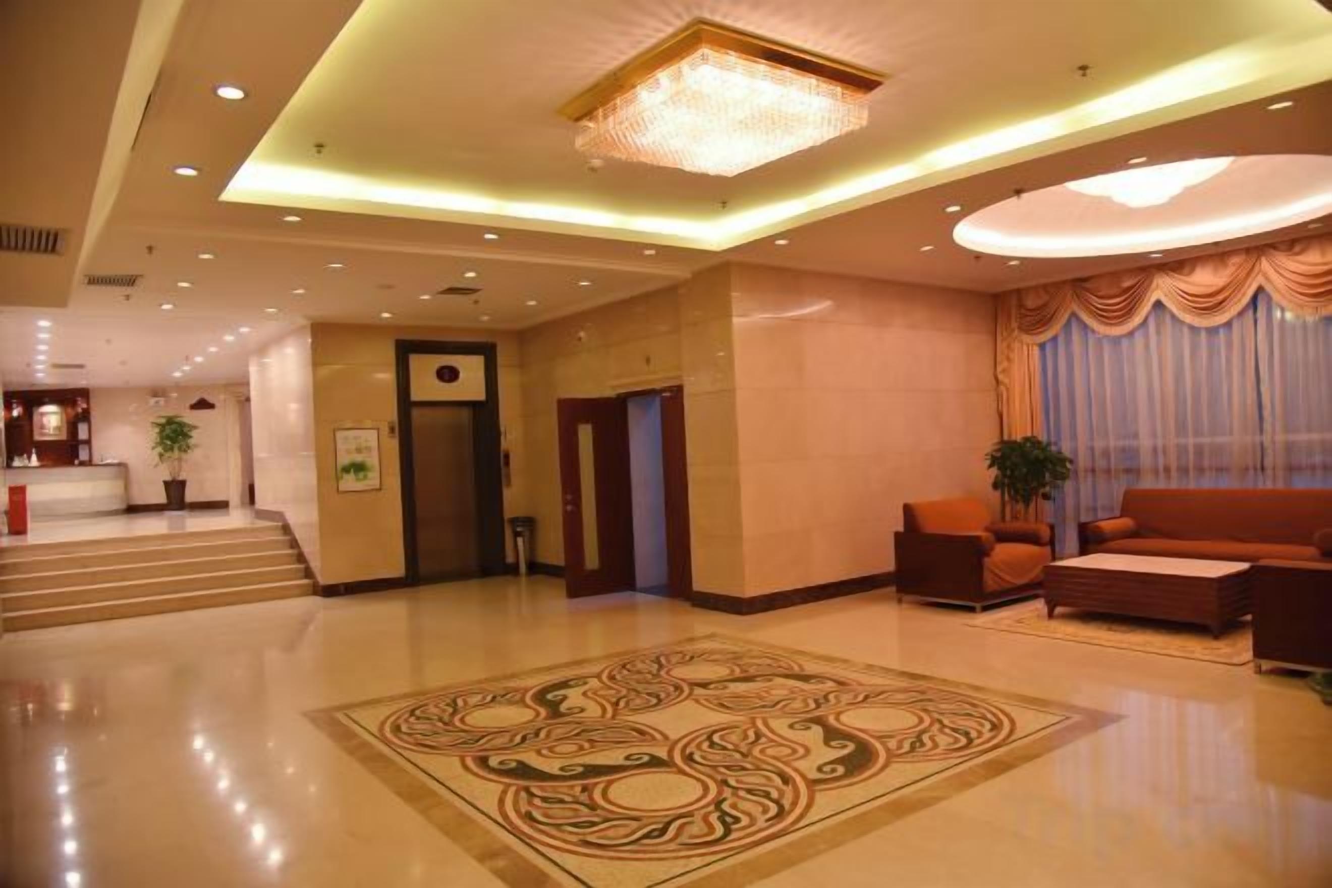 A hotel lobby with a reception desk, a staircase, and a seating area with a large rug.