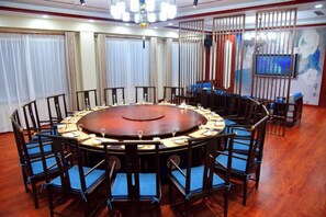 A conference room with a round table surrounded by chairs, a chandelier, and a large window with curtains. - Longshan Hotel (Handan)