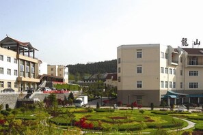 A multi-story building with a central courtyard, surrounded by greenery and a parking area. - Longshan Hotel (Handan)