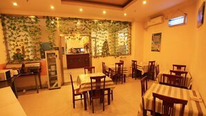 A dining area with multiple tables and chairs, a kitchen area with a refrigerator, and a wall decorated with green foliage. - GreenTree Inn Tianjin Xiqin Development District Dasi Meijiang Exhibition Center Hotel (Tianjin)