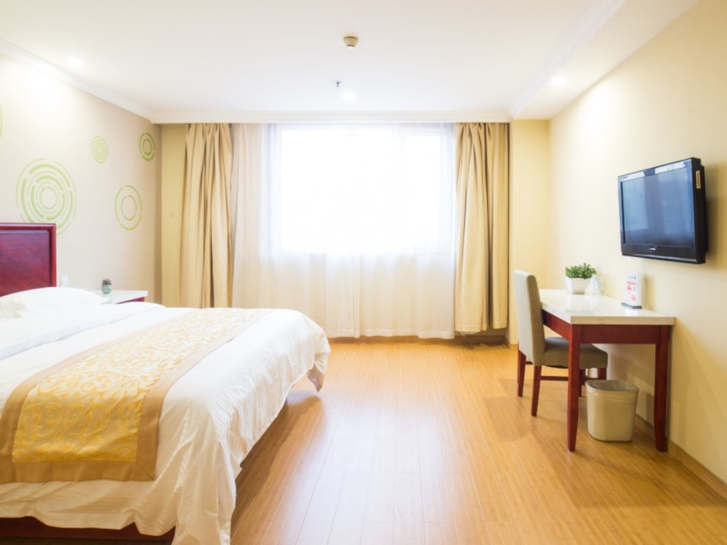 A hotel room with a bed, a desk, a chair, a television, and a window with curtains.