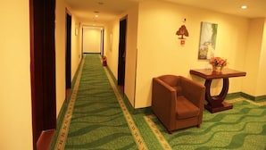 A hotel hallway with a green carpet, a brown armchair, a small table with a vase, and a painting on the wall. - GreenTree Inn Tianjin Xiqin Development District Dasi Meijiang Exhibition Center Hotel (Tianjin)