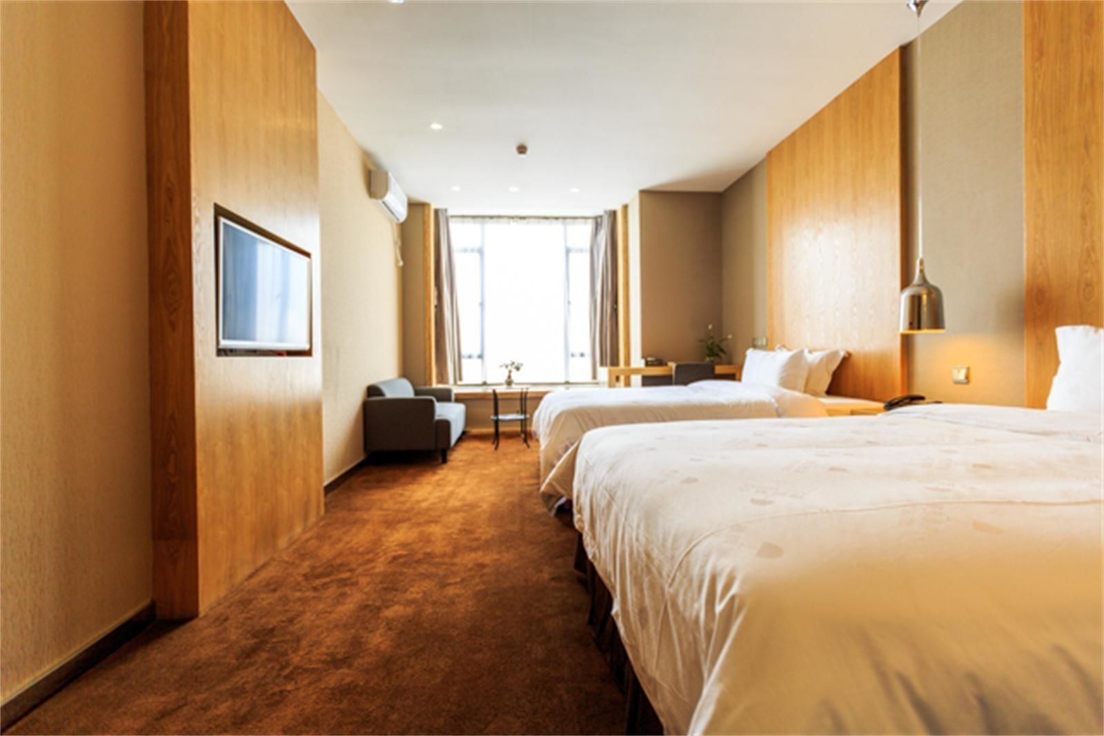 A hotel room with two beds, a sofa, a desk, and a window with curtains.