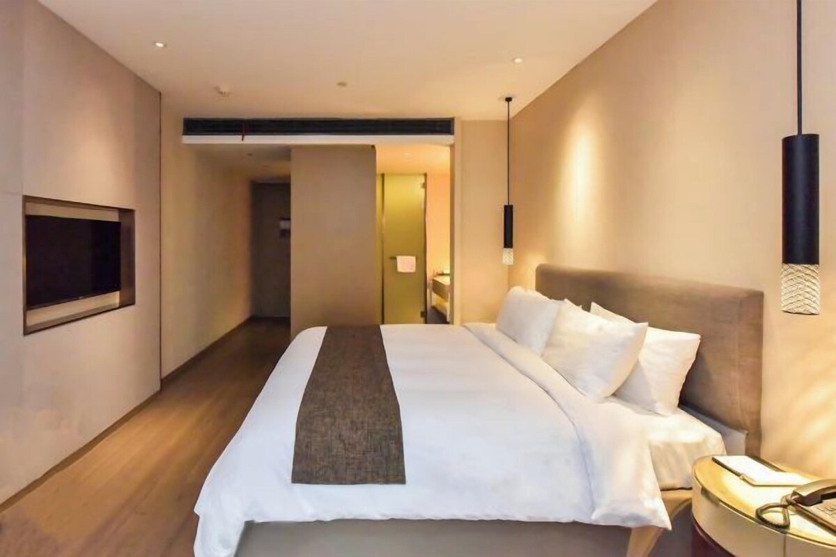 Une chambre d’hôtel moderne dotée d’un grand lit, d’un téléviseur à écran plat et d’une table de chevet avec une lampe.