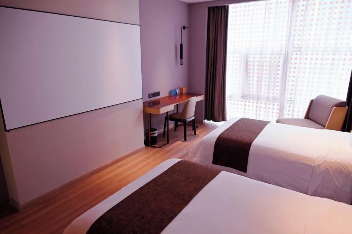 Habitación de hotel con dos camas, un escritorio, una silla y un ventanal grande.