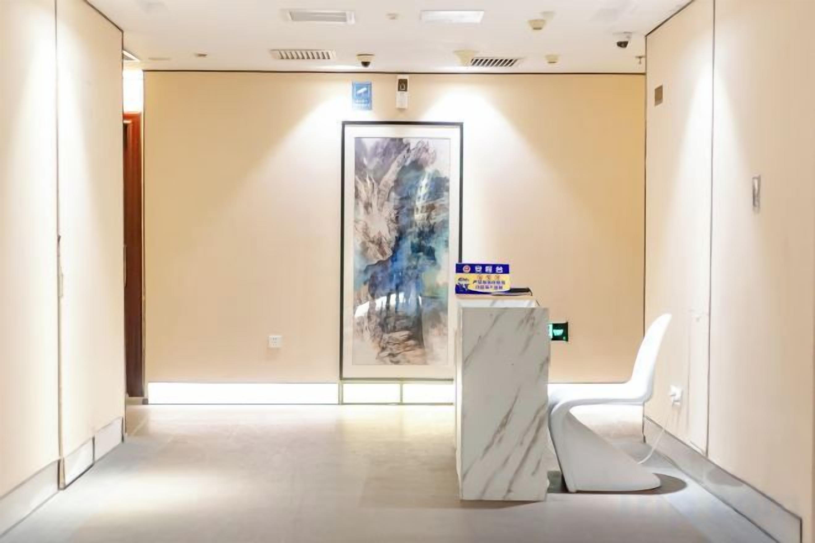 A hotel hallway with a reception desk, a chair, and a door with a painting.