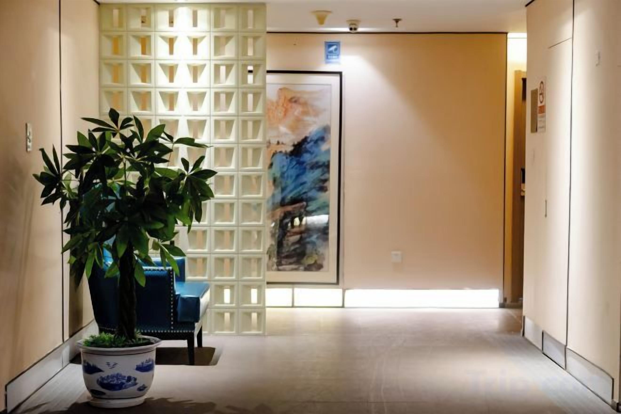 A hallway with a potted plant, a blue chair, a decorative screen, and a door with a painting.