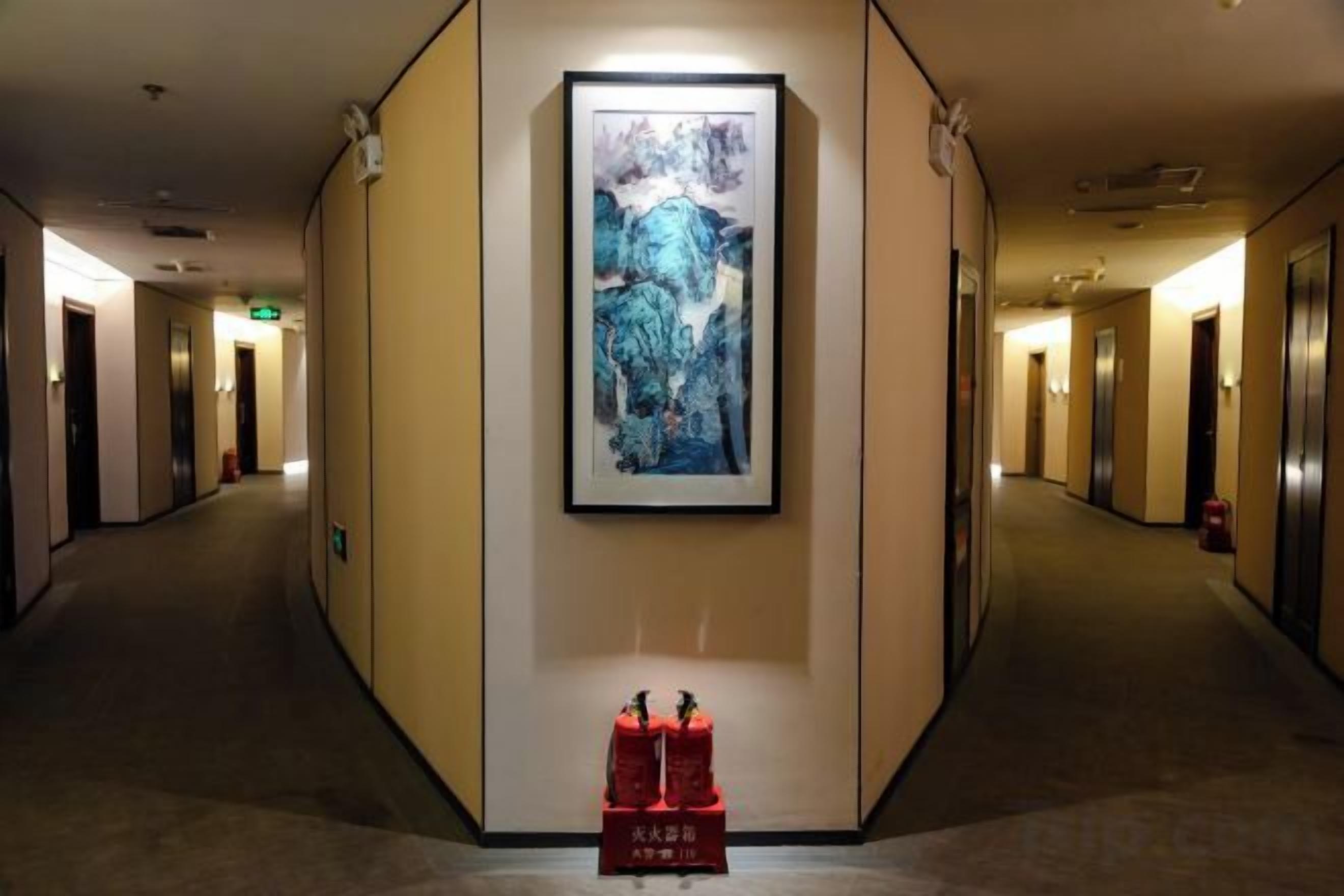 A hotel hallway with a framed artwork on the wall, a fire extinguisher, and a trash bin.