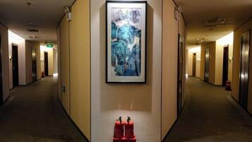 A hotel hallway with a framed artwork on the wall, a fire extinguisher, and a trash bin.