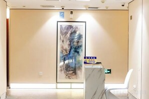 A hotel reception area with a marble counter, a framed abstract painting on the wall, and a door with an exit sign.