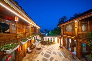 A traditional wooden building with a courtyard, stone flooring, and potted plants. - THREE WELLS INN (Lijiang)