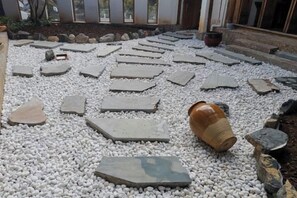 Une cour dallée de petits cailloux, avec des dalles de pierre et un grand pot en terre cuite.