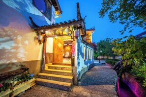 A traditional building with a staircase leading to an entrance, surrounded by greenery. - THREE WELLS INN (Lijiang)