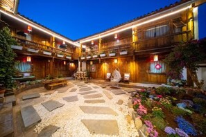 A courtyard with a stone floor, wooden benches, and potted plants. - THREE WELLS INN (Lijiang)