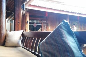 A wooden balcony with a bench and cushions, overlooking a traditional building with a tiled roof. - THREE WELLS INN (Lijiang)
