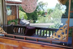 A traditional wooden bench with cushions, a decorative railing, and a view of greenery and buildings outside. - THREE WELLS INN (Lijiang)