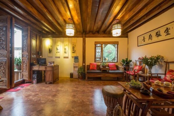 A traditional interior with wooden beams, a desk with a computer, a sofa, and a dining table with chairs.