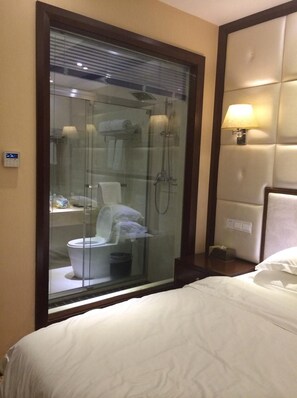 A hotel room with a glass-enclosed shower, a bed with white bedding, and a wall-mounted lamp. - Bali Holiday Hotel Shaoxing (Shaoxing)