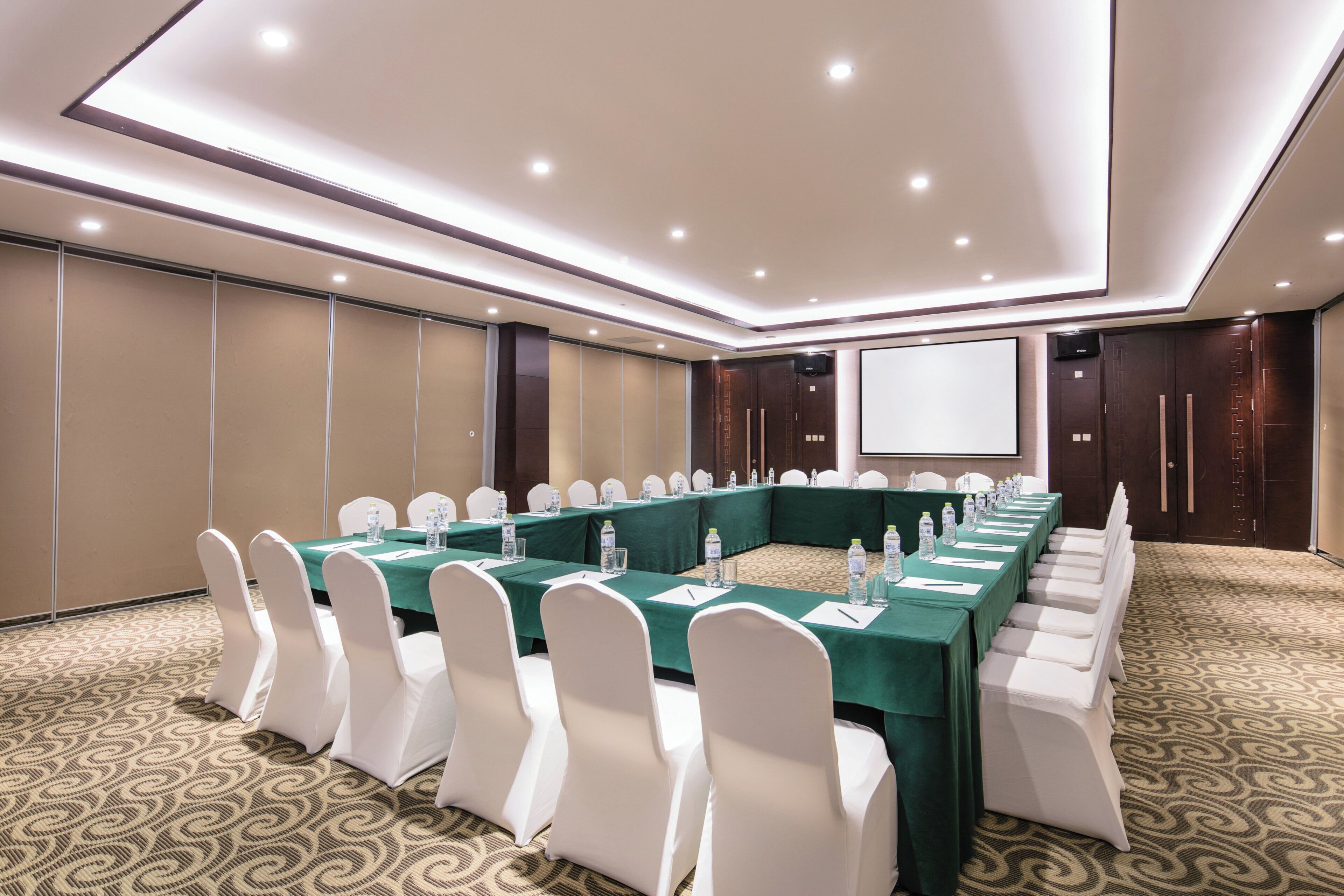 A conference room with a long table, white chairs, and a projector screen.