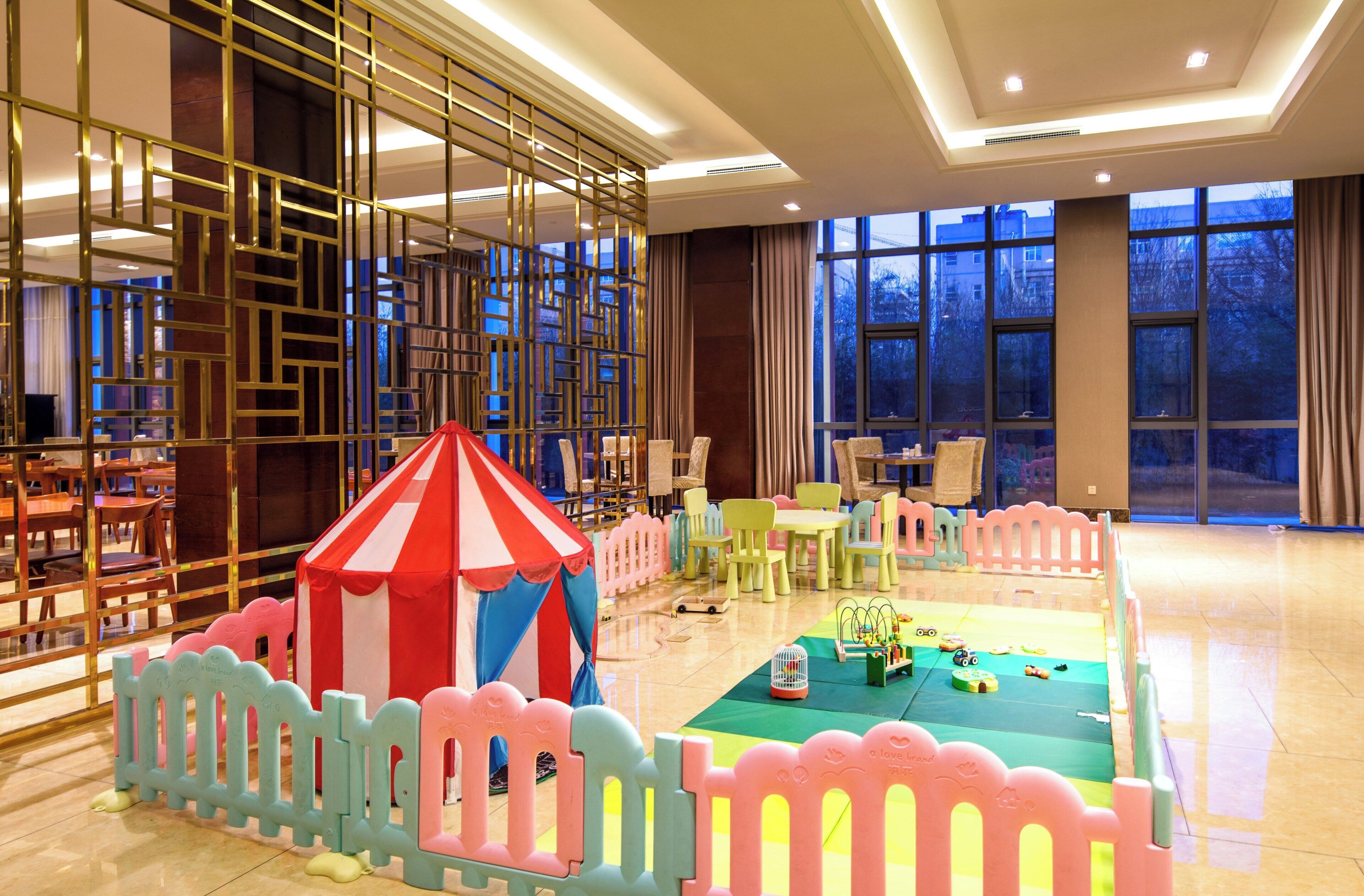 A children's play area with a small red and white striped tent, surrounded by a pink and blue fence, and various toys on the floor.