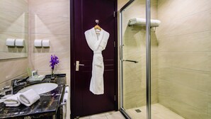 A bathroom with a dark wooden door, a glass shower enclosure, a marble sink, and a towel rack with a white robe. - Holiday Inn Beijing Airport Zone by IHG (Beijing)