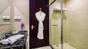A bathroom with a dark wooden door, a glass shower enclosure, a marble sink, and a towel rack with a white robe.