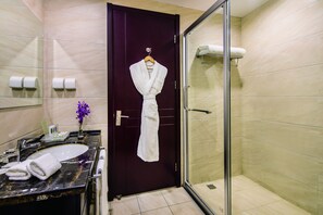 A bathroom with a dark wooden door, a glass shower enclosure, a marble sink, and a towel rack with a white robe. - Holiday Inn Beijing Airport Zone by IHG (Beijing)