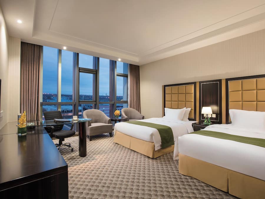 Habitación de hotel con dos camas, un escritorio, una silla y vista a la ciudad.