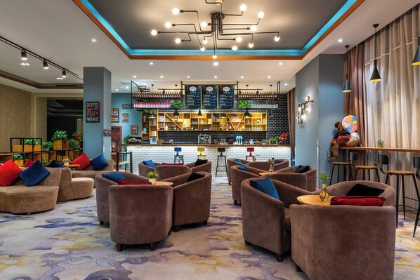 Vestíbulo de hotel con sofás, una zona de bar y una alfombra estampada.