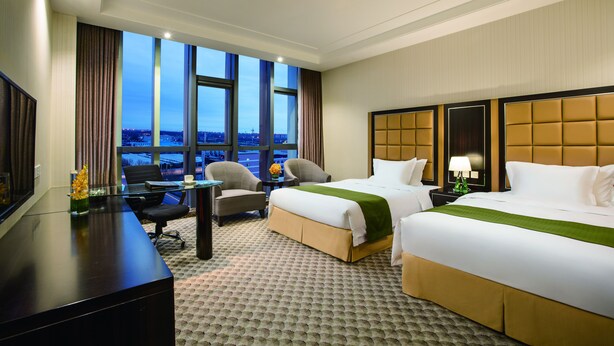 A hotel room with two beds, a desk, and a view of the cityscape. - Holiday Inn Beijing Airport Zone by IHG (Beijing)