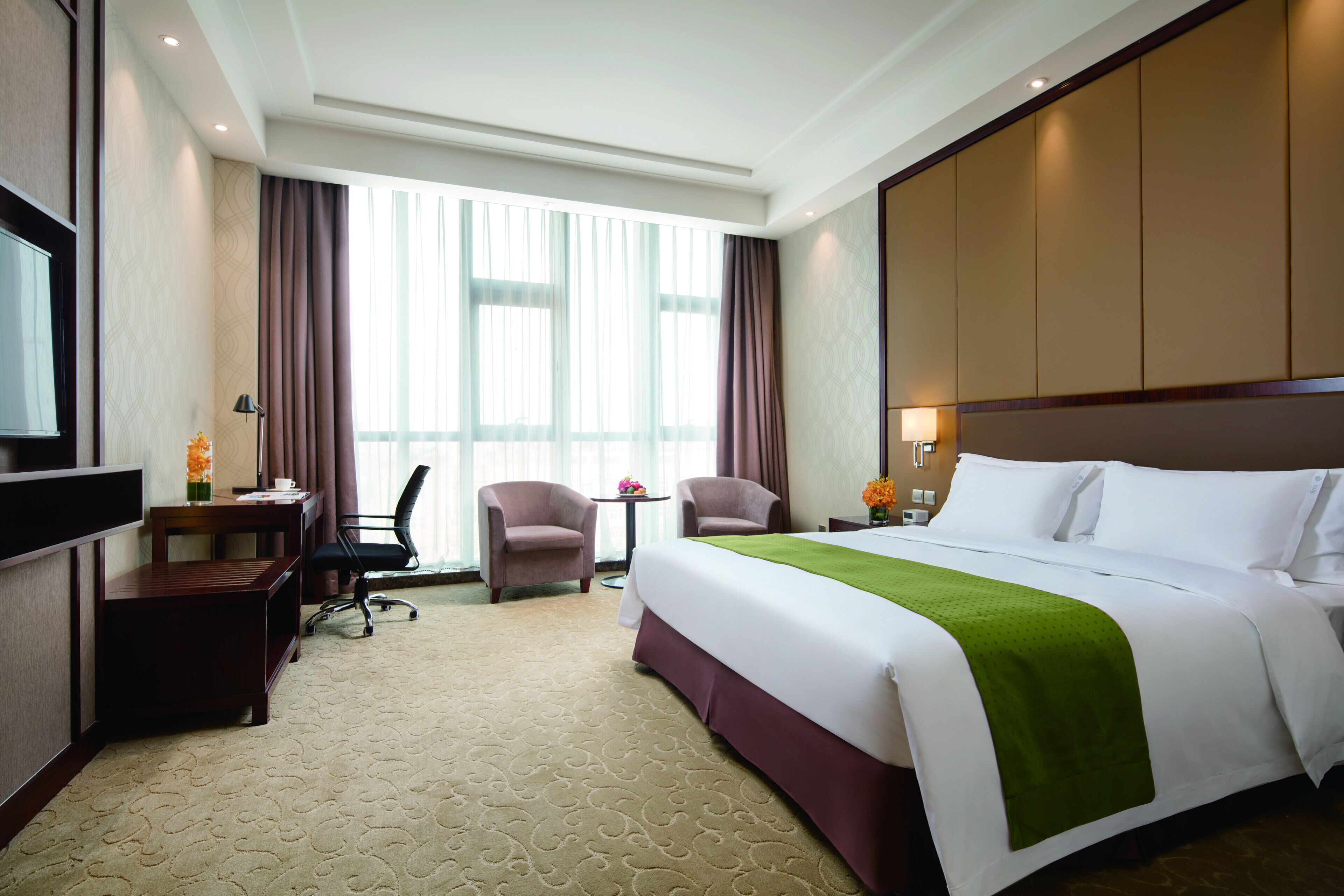 Habitación de hotel con una cama grande, un escritorio con silla, televisor y ventana con cortinas.