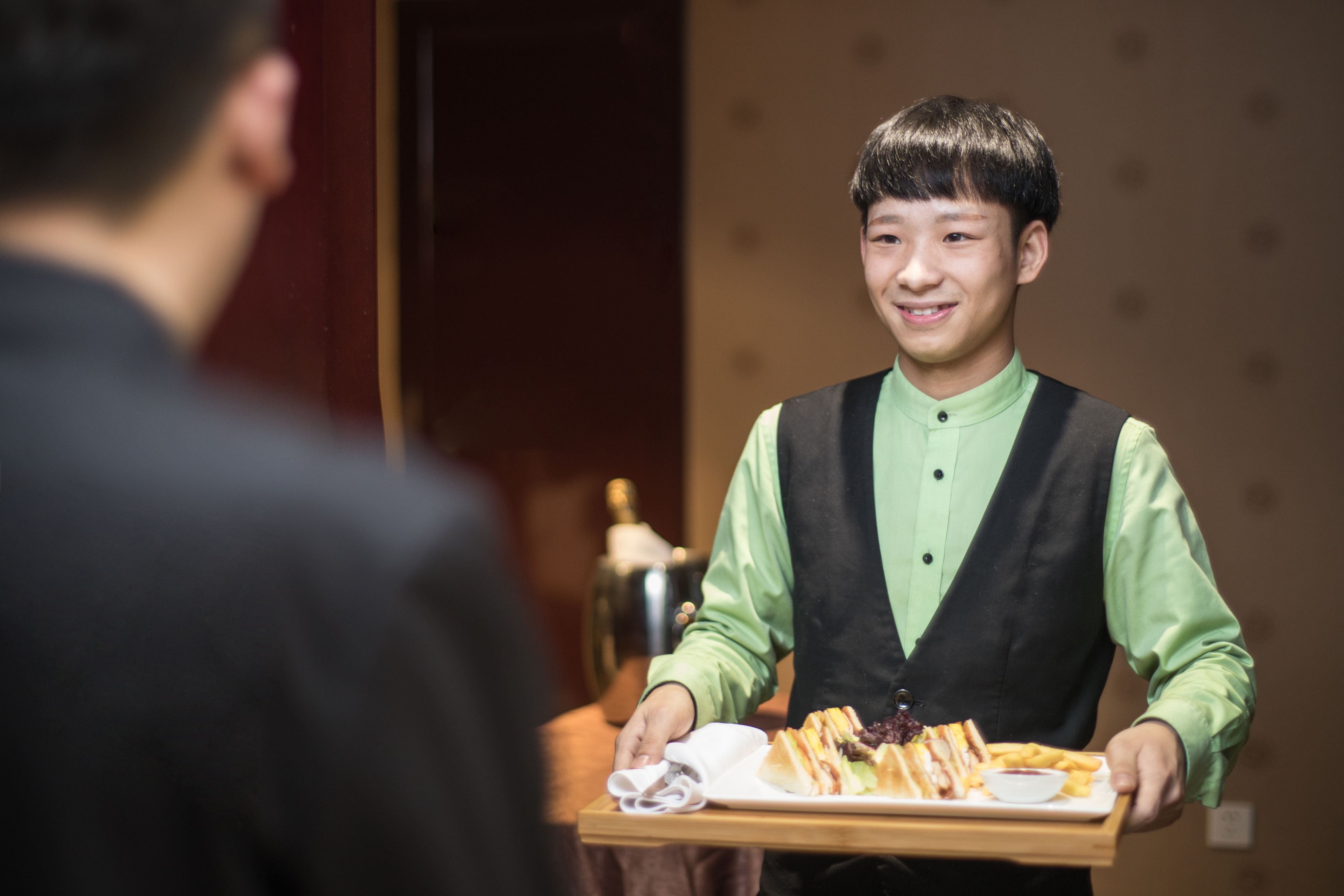 A waiter serving a tray with a sandwich, fries, and a drink to a guest.