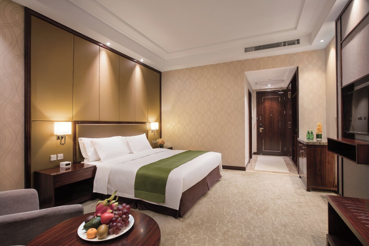 A hotel room with a bed, bedside table, fruit bowl, and a television.