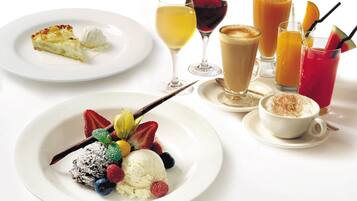 Una mesa con vajilla variada, incluyendo platos y bebidas, con un helado con frutos rojos, una porción de tarta y varios vasos.
