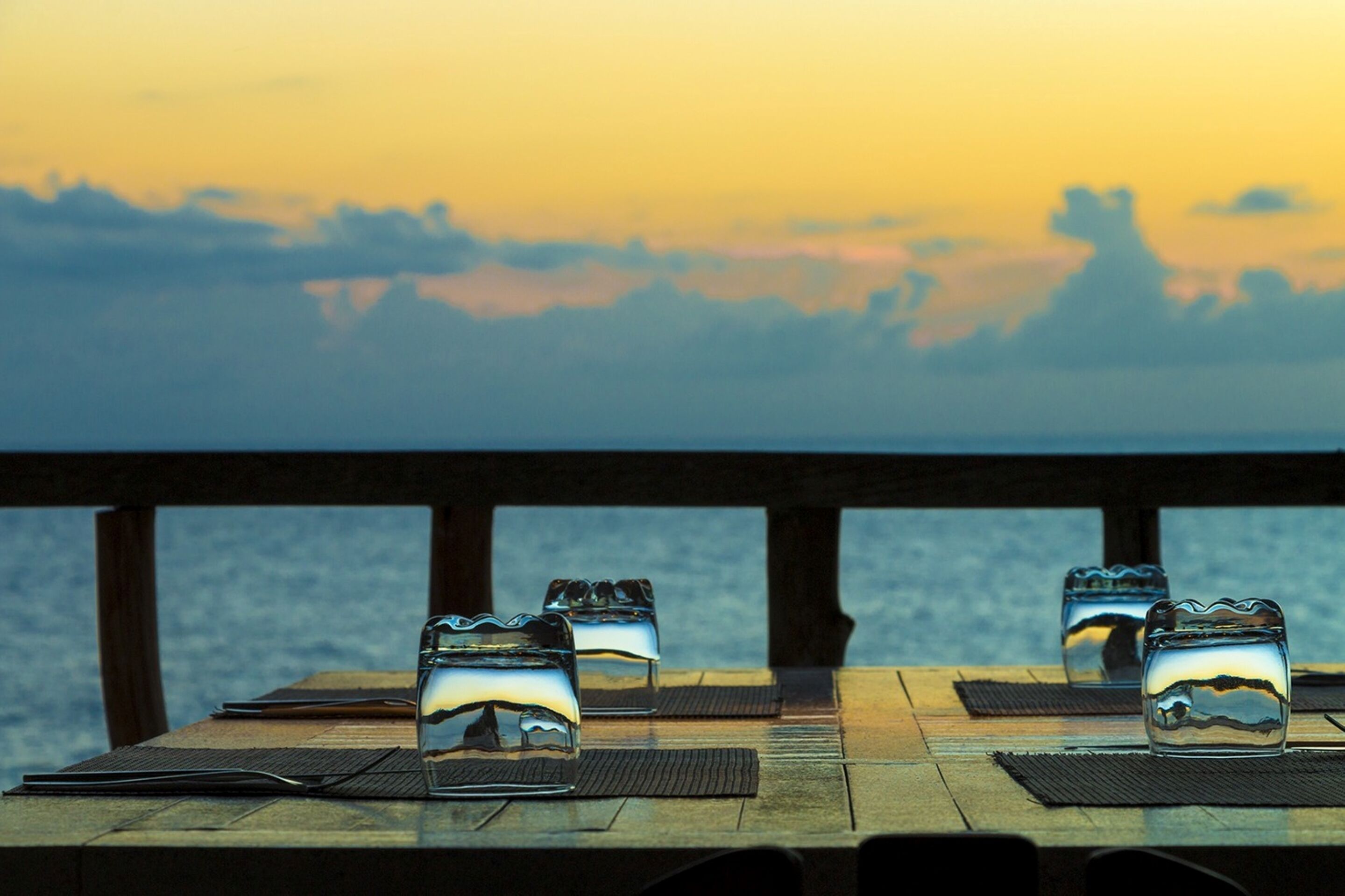 Un tavolo con tre bicchieri e un menu, vista su uno specchio d'acqua al tramonto.
