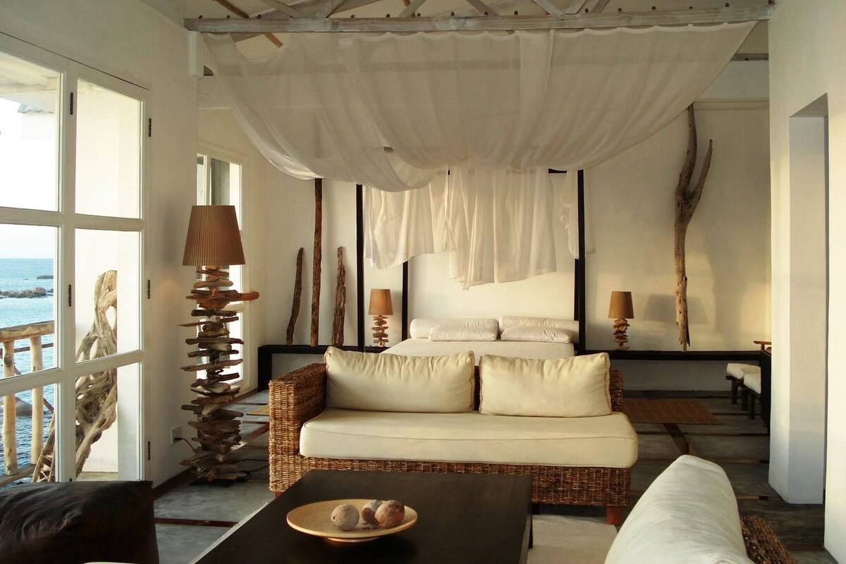 Una habitación con sofá de mimbre, una mesa de centro negra y una cama con dosel.