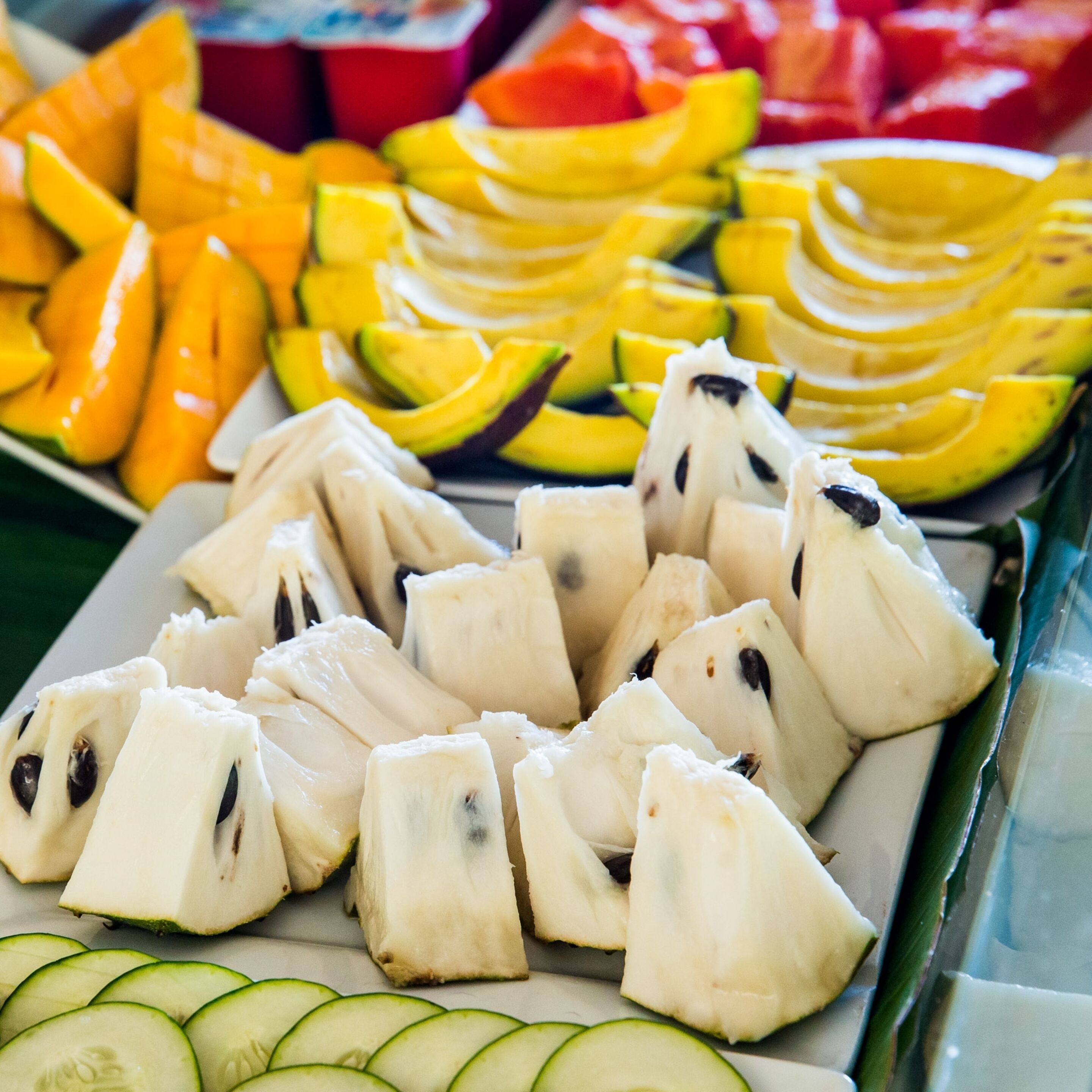 Eine Auswahl frischer Früchte, darunter Mangos, Bananen und Drachenfrucht, auf einer Schale angerichtet.