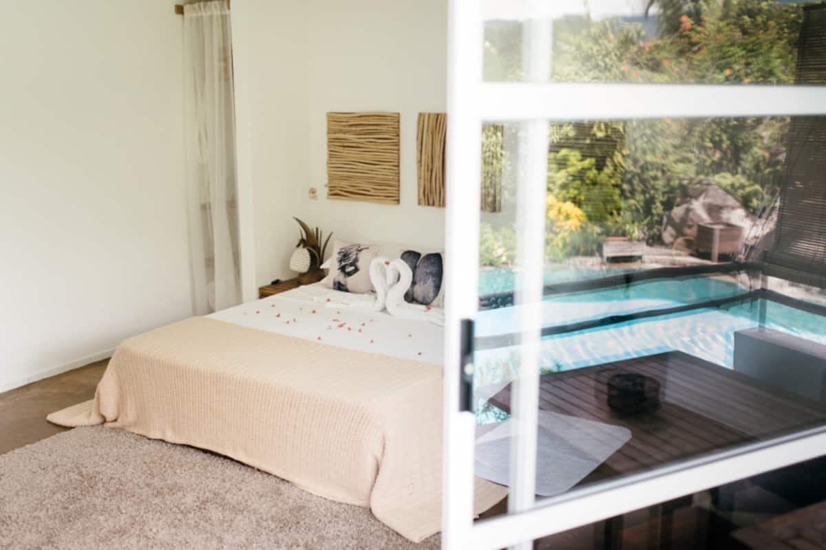 Un dormitorio con un ventanal grande que da a una piscina y jardín.