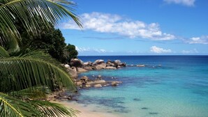 Una playa con agua turquesa cristalina, una orilla arenosa y grandes rocas.