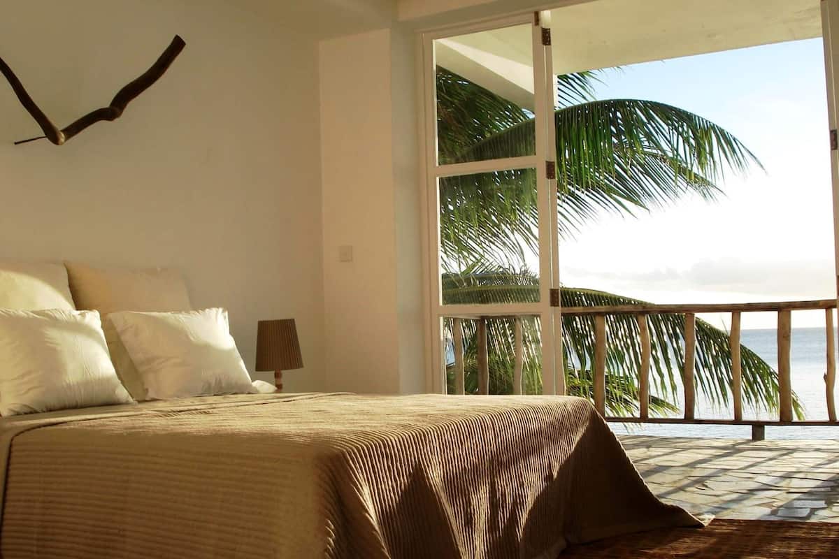 Un dormitorio con una cama grande, vistas al océano y un balcón con palmeras.