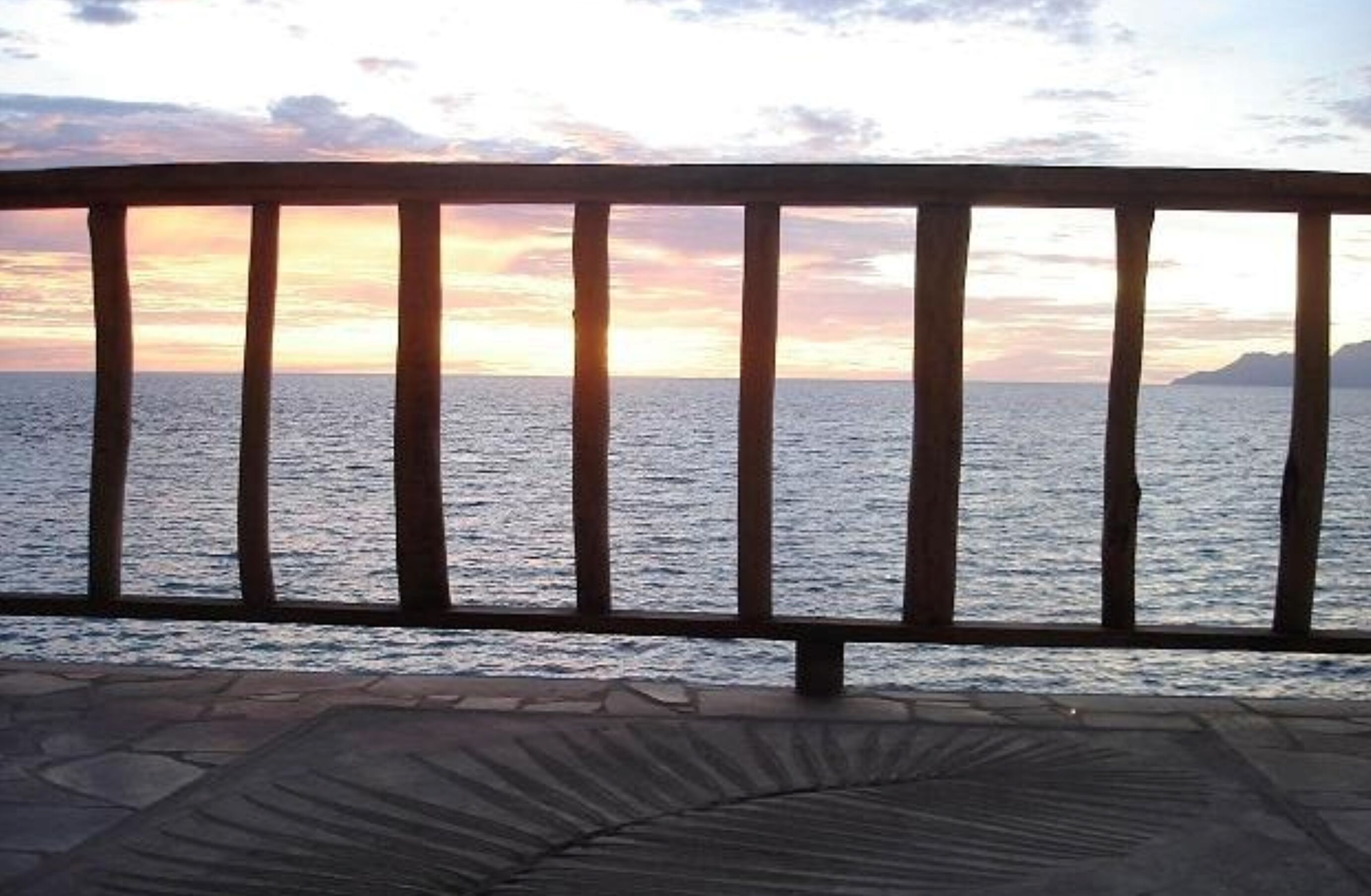 A wooden railing overlooking a body of water during sunset.