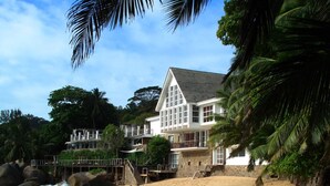 Una propiedad frente a la playa con una casa grande de color blanco, varios balcones y una costa rocosa.