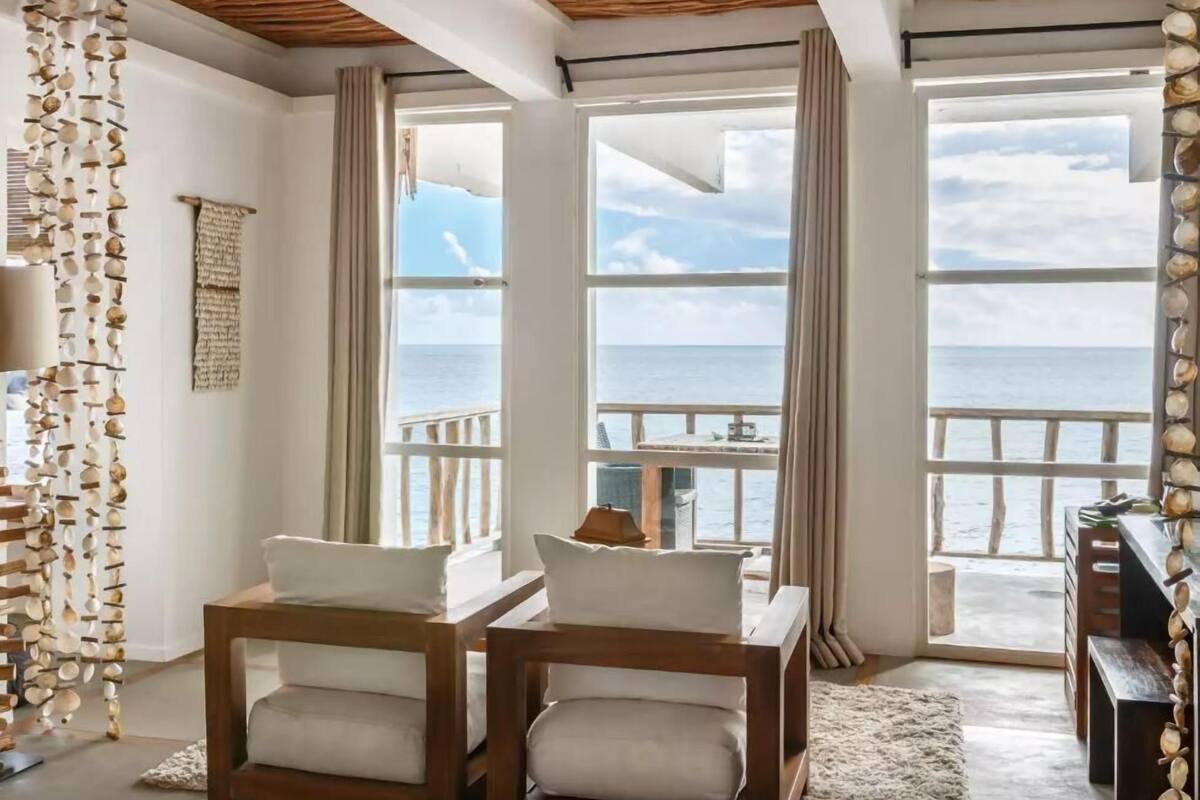 Habitación con vista al mar, techo de madera, ventanas amplias y una pared decorada con conchas.